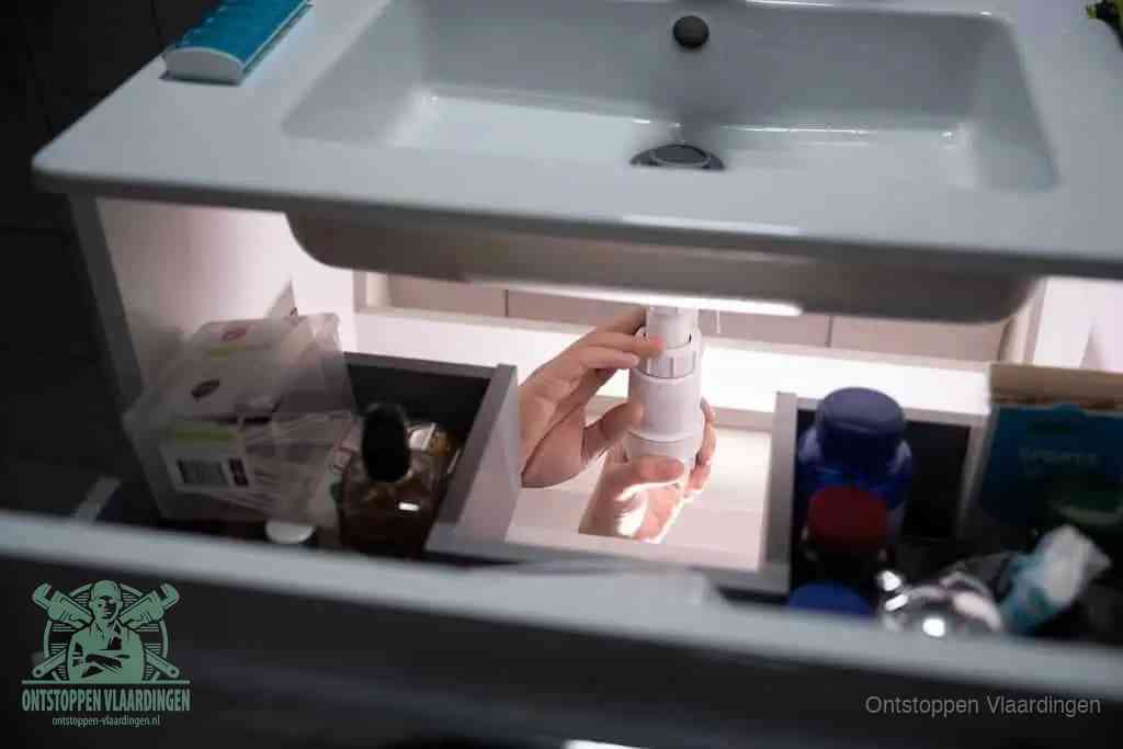 Een pompfles met zeep boven een wastafel, de heet water en afwasmiddel-methode om een vetprop in de afvoer los te maken in Vlaardingen