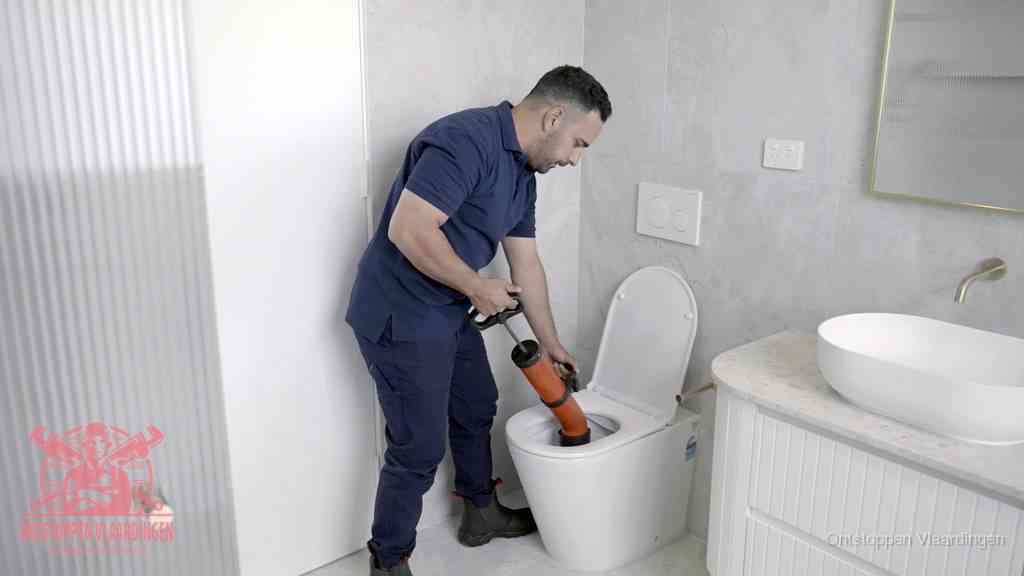 Een monteur buigt over een wandcloset en duwt met de hand een persluchtontstopper in de toiletpot om de verstopping handmatig los te maken in Vlaardingen