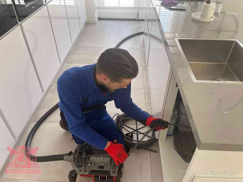 Een monteur ontstopt de keukenafvoer onder de spoelbak met een elektrische veermachine in Vlaardingen
