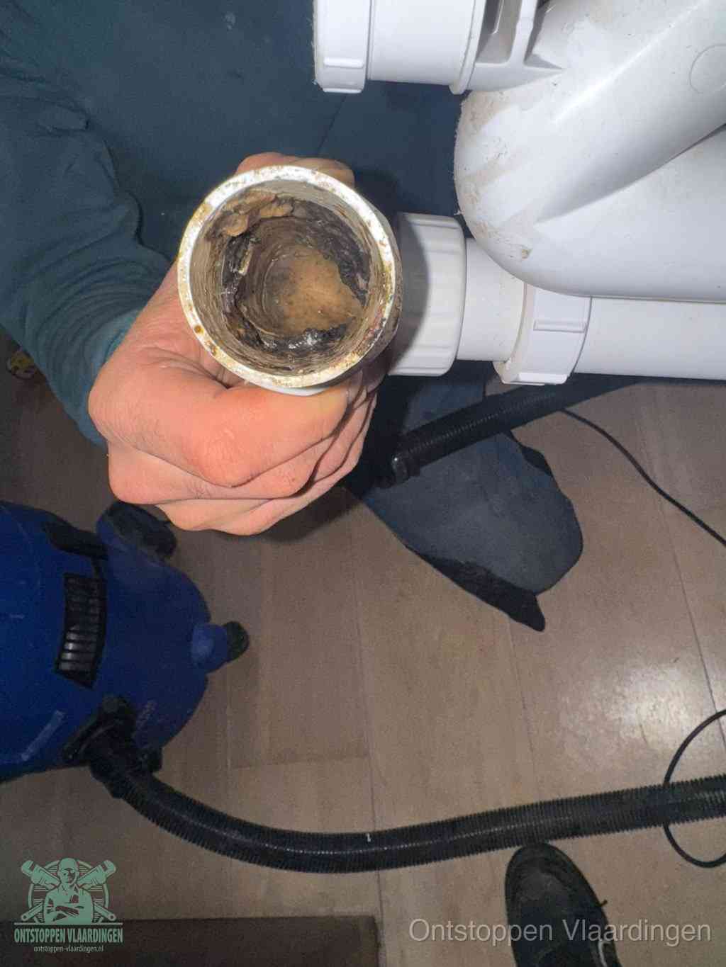 Een hand houdt een losgekoppeld PVC-afvoerbuisstuk vast dat van binnen volledig is dichtgeslibd met vet, vuil en aanslag, de meest voorkomende oorzaak van een verstopte afvoer in Vlaardingen