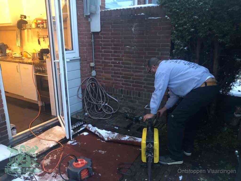 Een monteur werkt buiten bij een open riool-/grondput met een elektrische ontstoppingsmachine om een verborgen afvoerprobleem op te sporen in Vlaardingen