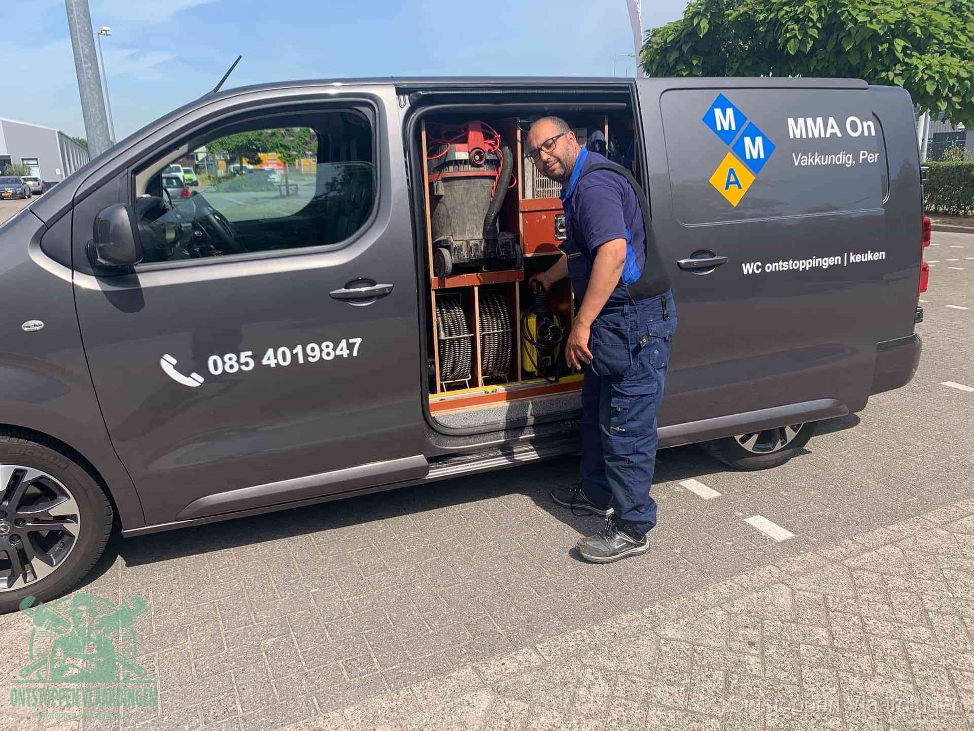 Een monteur bij de open schuifdeur van zijn bedrijfsbus op een parkeerplaats, klaar om de oorzaak van terugkerende afvoerverstoppingen aan te pakken in Vlaardingen