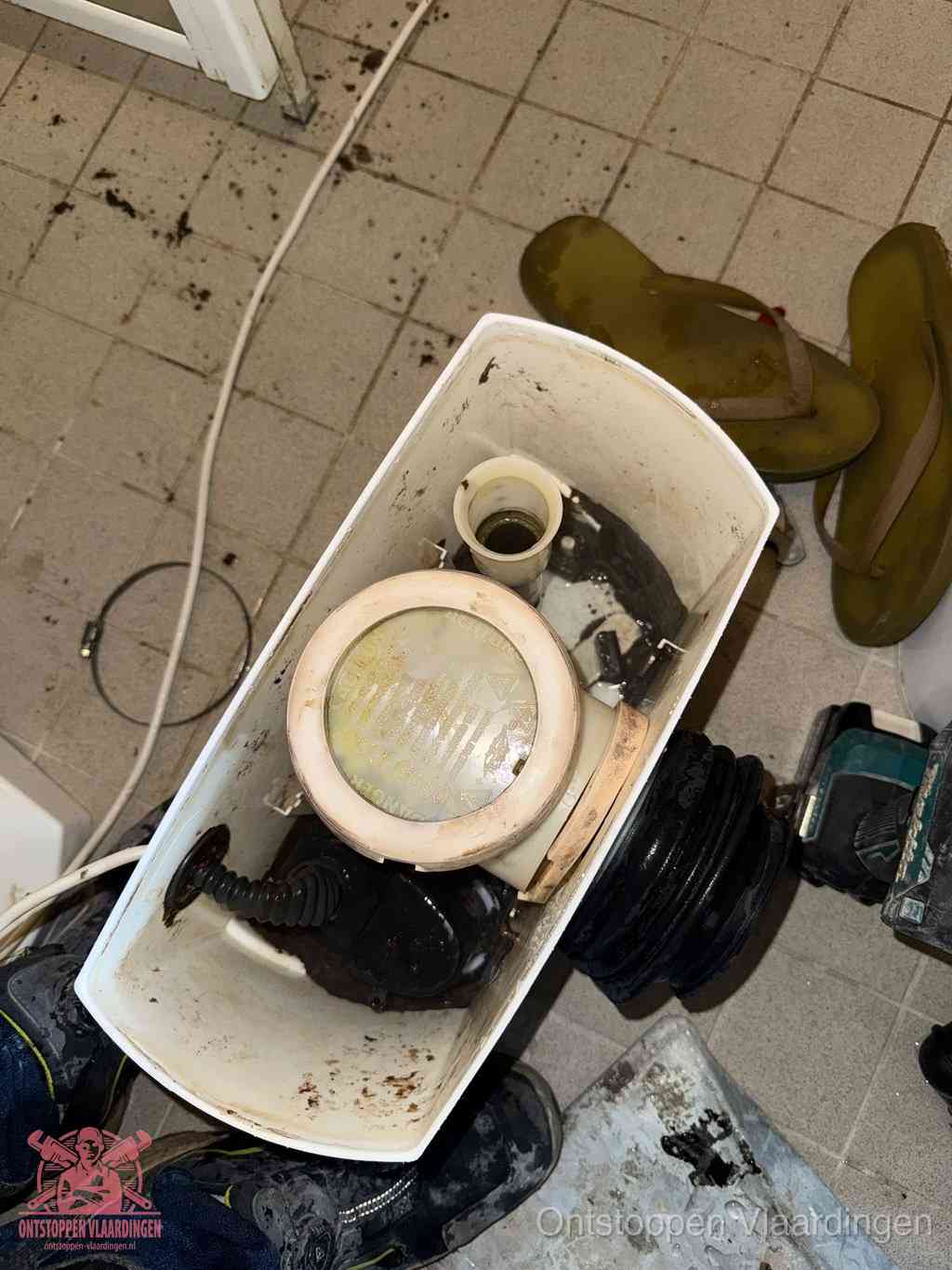 Een gedemonteerde toiletpot op de vloer met ontstoppingsveer en gereedschap ernaast, het verwijderen van een vastzittend voorwerp uit de wc in Vlaardingen