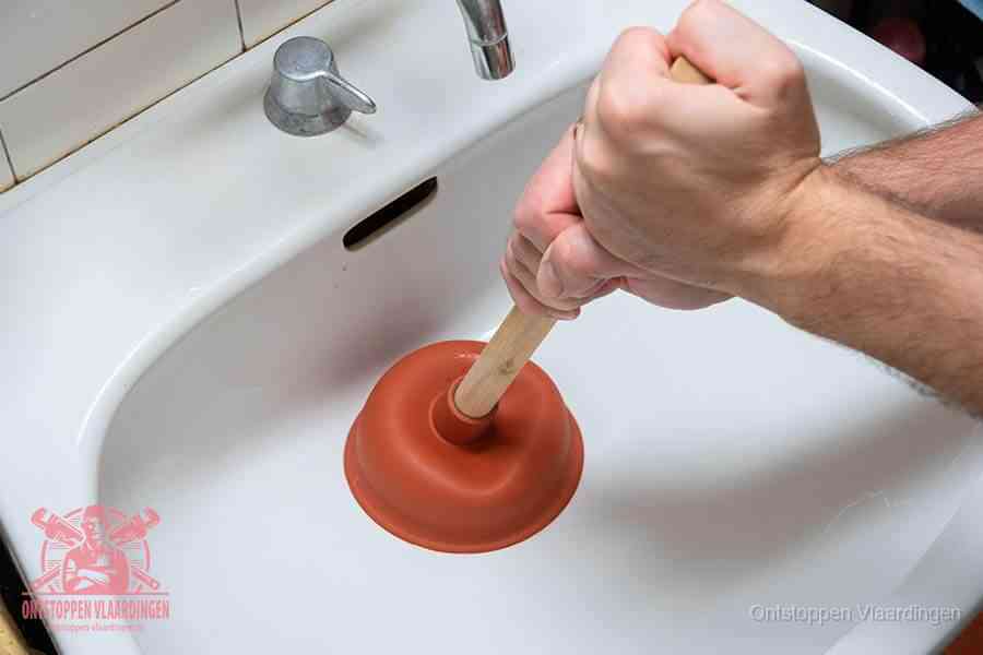 Twee handen gebruiken een rode rubberen plopper op een sanitair-afvoer om het toilet te ontstoppen in Vlaardingen