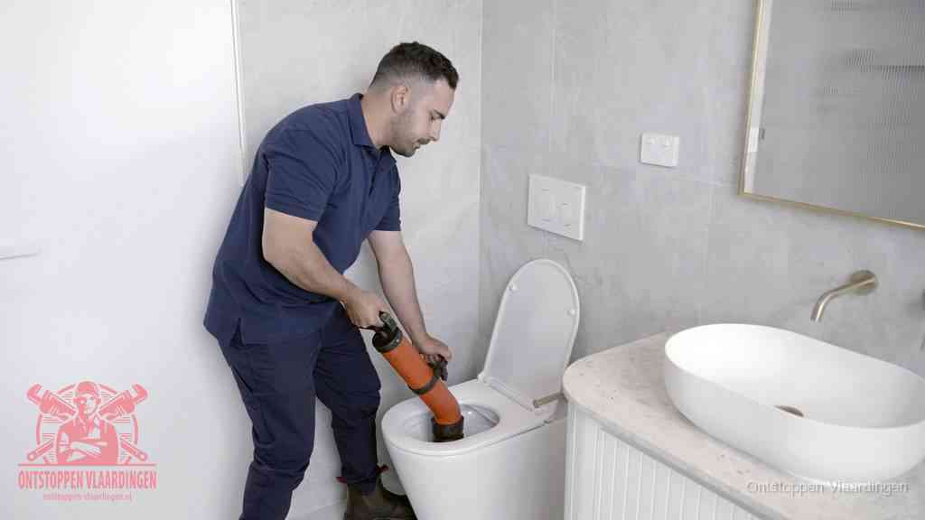 Een man gebruikt een handmatige luchtdruk-ontstopper in een modern betegeld toilet om zelf de wc te ontstoppen in Vlaardingen